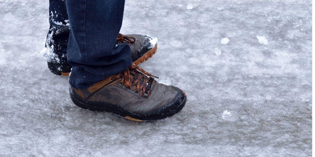 Erittäin liukkaalla kelillä  kannattaa valita jalkaan säänmukaiset kengät. Kuvituskuva kengistä jäisellä kadulla. 