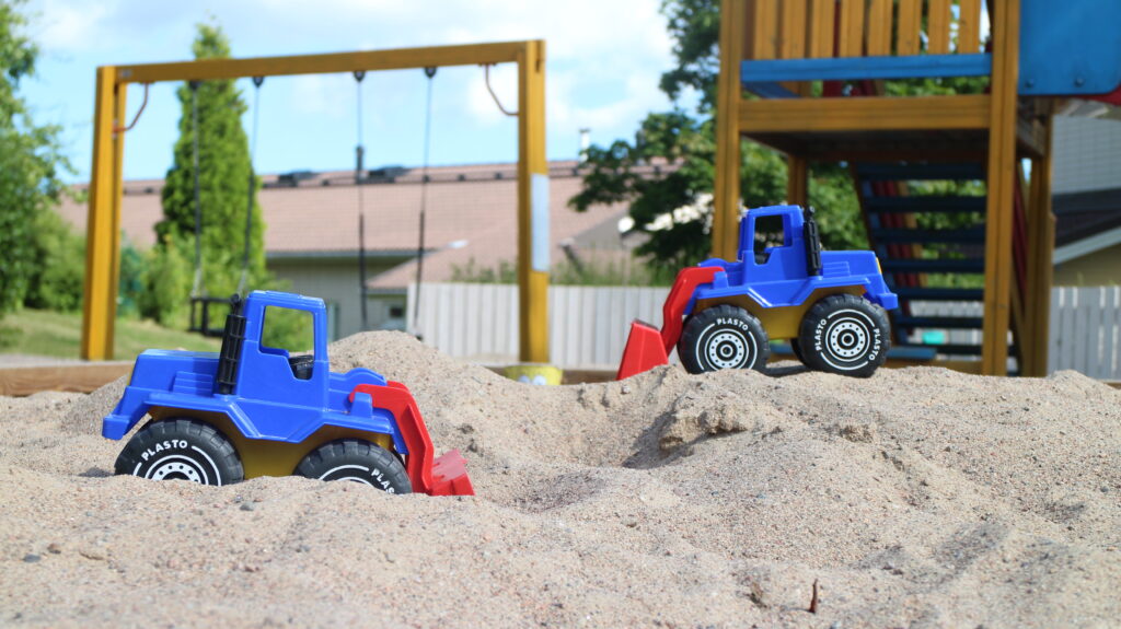 Kuvassa hiekkalaatikko, jonka taustalla näkyy taloyhtiön leikkikenttä. Kuvituskuva leikkipaikan turvatarkastus artikkelille. 