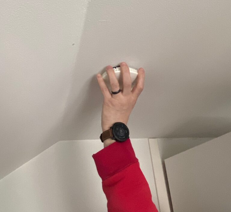 Kuvassa käsi kiinnittää palovaroitinta kattoon.